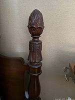Close-up image of intricately carved finial top post of the bed frame, showing detailed leaf and diamond pattern carving in dark wood finish.