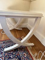 Photo showing white wooden side table with curved X-shaped legs and decorative rectangular top.