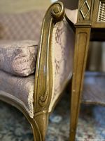 Close-up of carved armrest and legs of the vintage sofa, showing wood finish and upholstery.