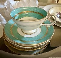 Close-up of turquoise and gold accented tea cup with matching saucers stacked below