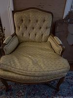 Front view of one upholstered chair showing tufted back, wooden frame detail, patterned green fabric upholstery, visible wear and fabric tear on the seat.