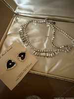 Photo of silver-tone necklace with clear imitation stones and black heart-shaped earrings on original card.