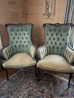 Front view of both oversized velvet upholstered side chairs together, showing the faded green velvet and carved wooden frames.