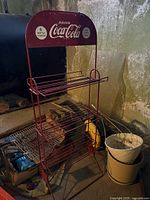 Full view of red vintage Coca-Cola metal stand with wire rack shelves and branded sign panel on top.