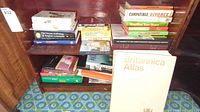 Photo of a wooden shelf with various books including Britannica Atlas prominently displayed in front.