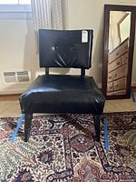 Front view of vintage mid century modern black vinyl chair placed on patterned rug indoors, showing chair seat and button tufting on backrest.