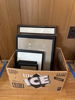 Box containing multiple picture frames of various sizes and colors including black and dark brown