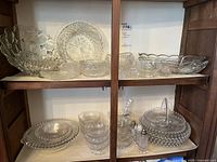 Wide view of upper and middle shelves showing multiple Imperial Glass Candlewick pattern pieces including several bowls, covered dish, salt and pepper shakers, and serving dishes with bead detailing on edges.