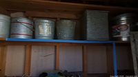 Five galvanized metal buckets and a vintage metal gas can on a shelf in a wooden structure, taken from a tilted angle.