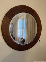 Front view of the square wooden frame mirror with round reflective glass, hanging on a wall.