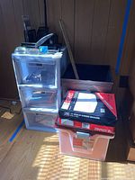 Two plastic three-drawer chests, wooden chest, table lamp, and boxes of business envelopes stacked in a pile.