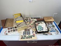 Overall view of stamps laid on a table including storage box, stock book, loose sheets, and small box of stamps