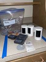 Three white Ring Stick Up Cams, five battery packs, mounting plates and spacers in a bag on countertop