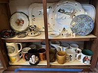 Wide view of cabinet shelves with assorted trays, plates, and coffee mugs arranged on two levels. Top level displays several decorative trays and plates, bottom level has multiple mugs organized side by side.