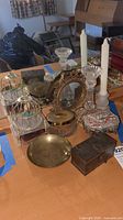 Full view of the lot on table showing brass bowl, glass candlesticks, mirror, glass jar, trinket boxes, and music box with bird cage