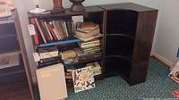 Two wooden bookcases displayed side by side, one rectangular and one curved corner piece, both containing books and showing surface wear