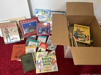 Wide view showing most of the children's books collection including books stacked beside and inside a cardboard box