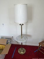 Full view of the vintage marble base table lamp with brass tarnished base and off-white lampshade on a red carpet.