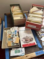 Photo of two boxes filled with multiple paper envelopes containing stamps and a smaller tray with loose stamps.