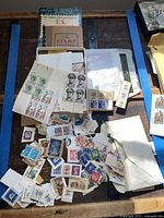Overview of stamps spread on table including loose stamps, partial sheets, and a stamp collector's guide book