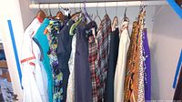 Full view of multiple vintage women's clothing items hanging on a single clothing rack, including dresses and skirts in various colors and patterns.