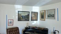 View of five framed pieces of wall art displayed on a wall above a piano. Includes people, landscape, abstract and bird themes. Frames vary in style and color.