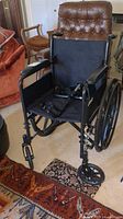 Front view of the wheelchair showing black fabric seat, armrests, and foot supports.