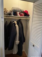 Full view of closet showing four winter coats hanging and shelves above with scarves, hats, and other winter accessories such as slippers and umbrellas.