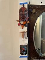 Three wooden carved wall art pieces hanging vertically including colorful tribal mask, wooden bull head, and carved face below