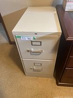 Front view of a beige metal two-drawer file cabinet with handles and label holders on drawers.
