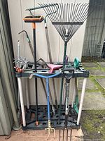 Full view of garden tools upright in rack showing various handles and tool heads including rakes, pitchfork, cultivator, and brushes.