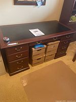 Full front view of the dark wood executive desk showing six drawers and black leather top insert, along with cardboard boxes stored beneath (not included).