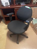 Front and side angle of black office chair showing fabric seat, armrests, and five leg base with rollers.