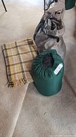 Image showing yellow plaid throw blanket, green sleeping bag in compression sleeve, and gray carrying bag containing air mattress.