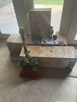 Artificial Christmas tree boxes stacked with decorative broom in front.