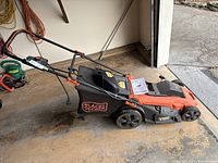 Side view of the Black & Decker corded electric lawn mower showing the grass catcher and handle with orange safety trigger.