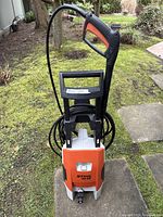 Front view of unit upright on concrete slab in backyard, hose wrapped around handle