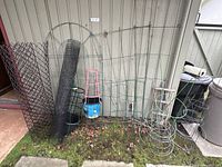 Overview of assorted garden accessories including tomato cages, trestles, wire fencing and plant covers leaning against a wall.