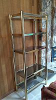 Full view of tall metal brass-coloured shelf unit with four smoked glass shelves, missing top shelf