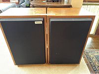 Pair of wooden framed speakers with black fabric covers placed side by side on floor.