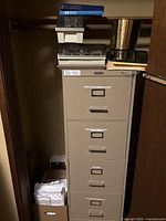 Photo of full beige 4-drawer metal file cabinet with items on top and copy paper stacked at bottom