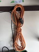 Coiled orange extension cord hanging against a wall showing plug and connector.