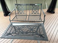 Metal outdoor love seat and matching table with glass top set on wooden deck. Includes 4 small throw cushions.