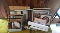 Various picture frames arranged leaning against a wall with colorful artwork and rolled prints in front
