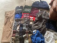 Showing large beige pants on left alongside folded assorted vintage T-shirts and sweaters in colors black, green, blue, red, and navy.