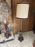 Tall floor lamp with beige shade and glass shelf on carved wooden base