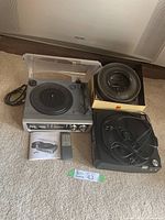Photo showing Kodak slide projector, two Kodak circular slide cartridges, Brookstone iConvert USB turntable with dust cover, remote control and user manual on carpeted floor.