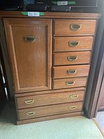 Front view of oak tall boy dresser showing five drawers on right and one cabinet door on left with brass handles.
