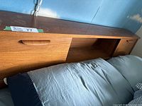 Side view of solid wood headboard attached to metal bed frame showing sliding door with recessed handles, mattress in front