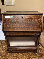 Front view closed showing drop-front writing panel with brass lock and string-tied key, narrow drawer above glass case and bottom storage drawer
